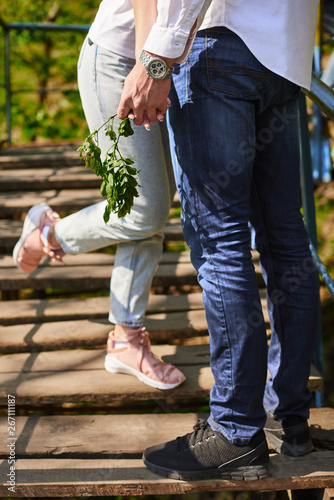 legs of young hugging couple on stairs in green park - two pairs of hands in love tenderly hold together