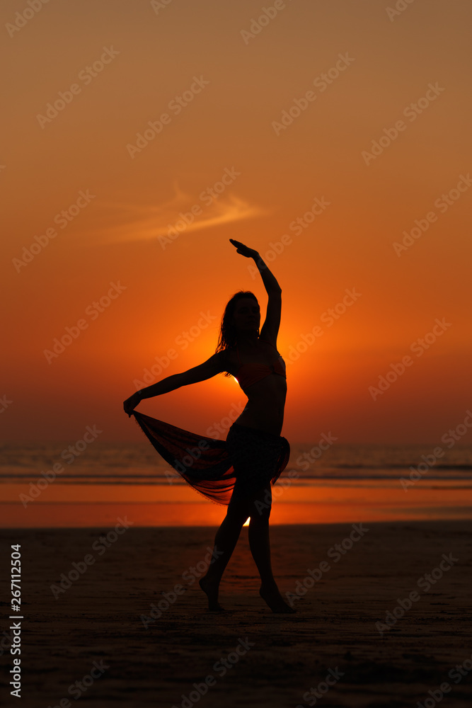 Silhouette of a woman with a beautiful figure at sunset on the beach with a beautiful sky. Orange sunset reflected in the sea. Amazing landscape. Concept of inspiration, relaxation and healthy.