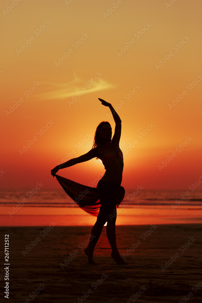 Woman dancing on the beach. Sunset and silhouette.