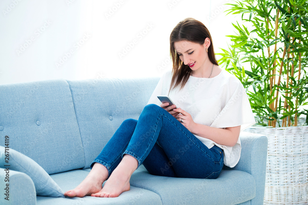 young woman sitting on a sofa while playing with her smartphone