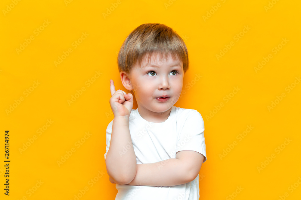 Portrait of cute handsome blonde little boy with finger pointed up. Little child has idea. Kid isolated on yellow blackground. Success, bright idea, creative ideas Portrait of cute handsome blonde little boy with finger pointed up. Little child has idea. Kid isolated on yellow blackground. Success, bright idea, creative ideas