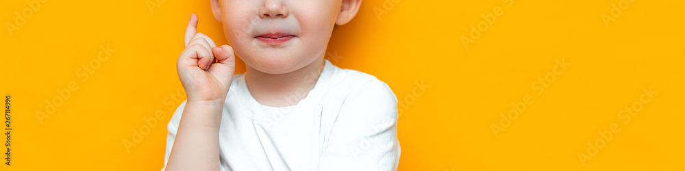 Fototapeta premium Portrait of cute handsome blonde little boy with finger pointed up. Little child has idea. Kid isolated on yellow blackground. Success, bright idea, creative ideas