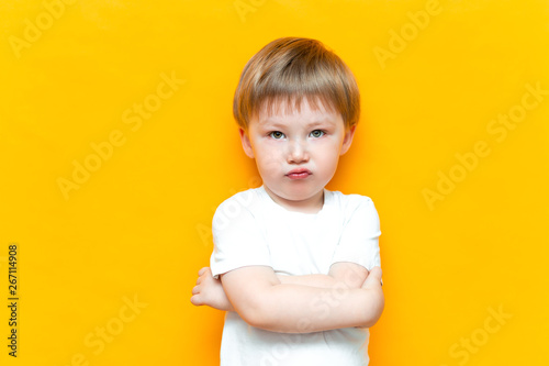 Portrait of angry little boy with arms folded isolated on yellow background. Sad and unhappy child. Upset toddler boy