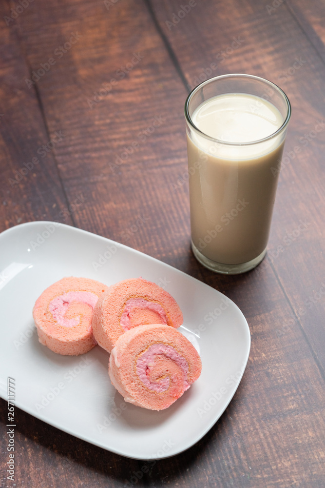 Strawberry cake roll on white dish and milk with wood background. Strawberry cake roll on white dish and milk with wood background.