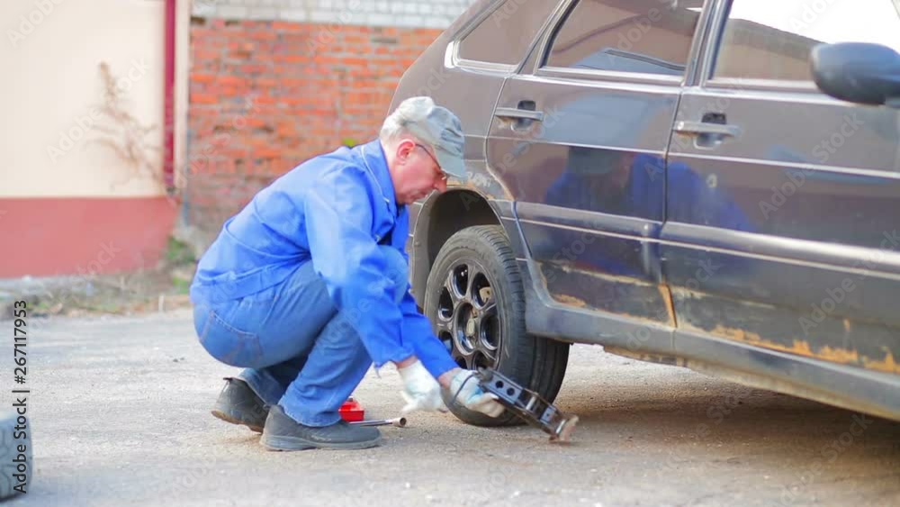 A man with a jack lowers the car to the ground. A man with a jack lowers the car to the ground.