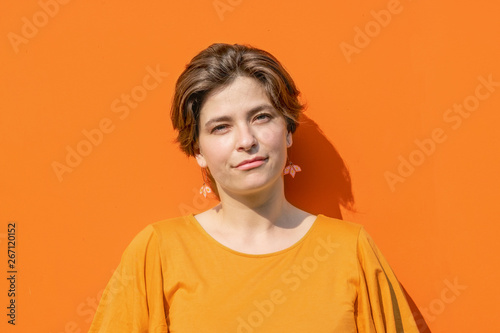 Beautiful young brunette woman portrait looking at camera. Orange colored metal texture background with space for text and design. Close up image of real people. Head shot. 