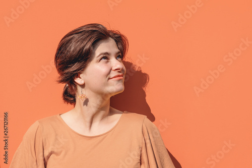 Beautiful young brunette woman portrait looking aside of camera. Beige colored metal texture background with space for text or design. Close up image of real people. Head shot. 