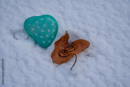 Two gold rings next to green heart shaped stone on the snow.