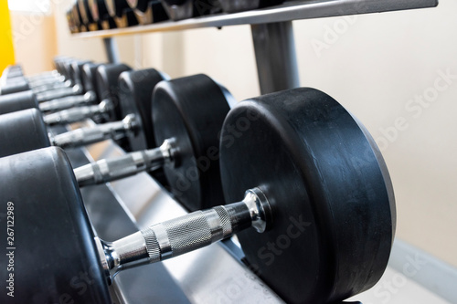 Black dumbbell set on rack close up in sport fitness center weight training equipment concept