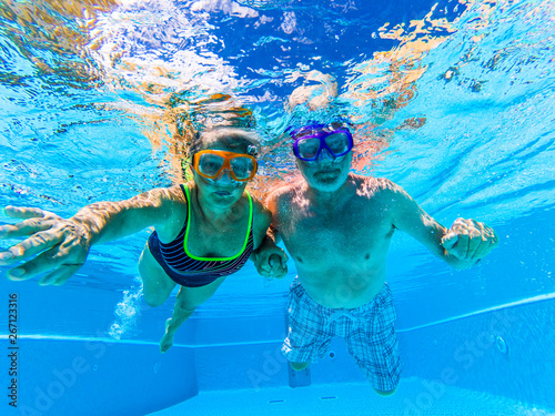 Adult people senior couple have fun swimmin in the pool underwater with coloured funny diving masks - dive concept and active retired man and woman enjoying the lifestyle - blue water and adults