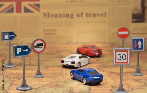 Travel concept. Toy cars on vintage World map with road sign. Newspaper as a background.