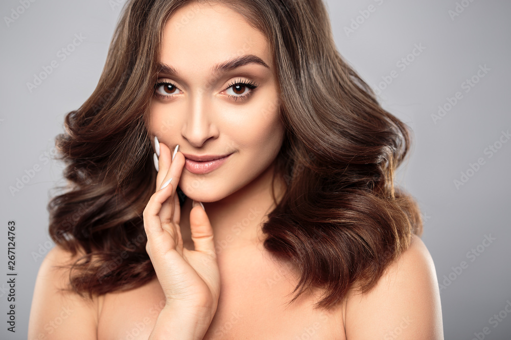 Brunette girl with healthy curly hair and natural make up . Beautiful model woman with wavy hairstyle .Care and beauty