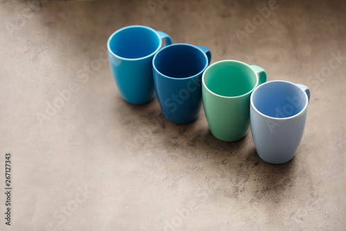 four tea mugs of different colors on a gray background © Дмитрий Ткачук