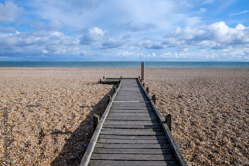 Fototapeta premium long straight wooden pathway on pebble beach leading to the sea