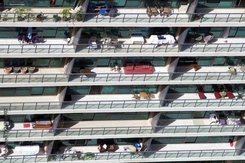 Aerial view of balconies aligned on a modern facade. Many items are visible, barbecues, tables, armchairs, plants...
