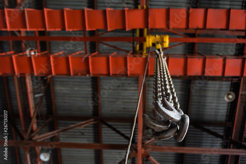 Фотография Metal hooks suspended on long chains of a monorail hoisting crane inside an industrial workshop, closeup