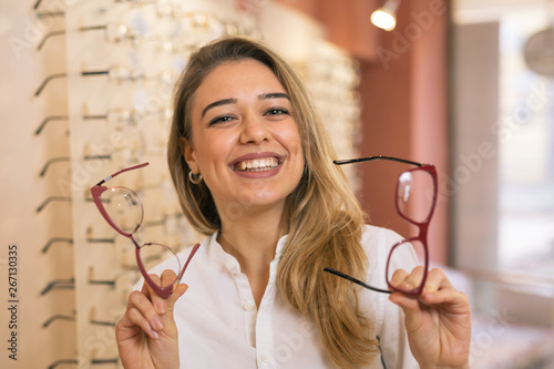 pretty smiling woman choosing eye glasses in optic store