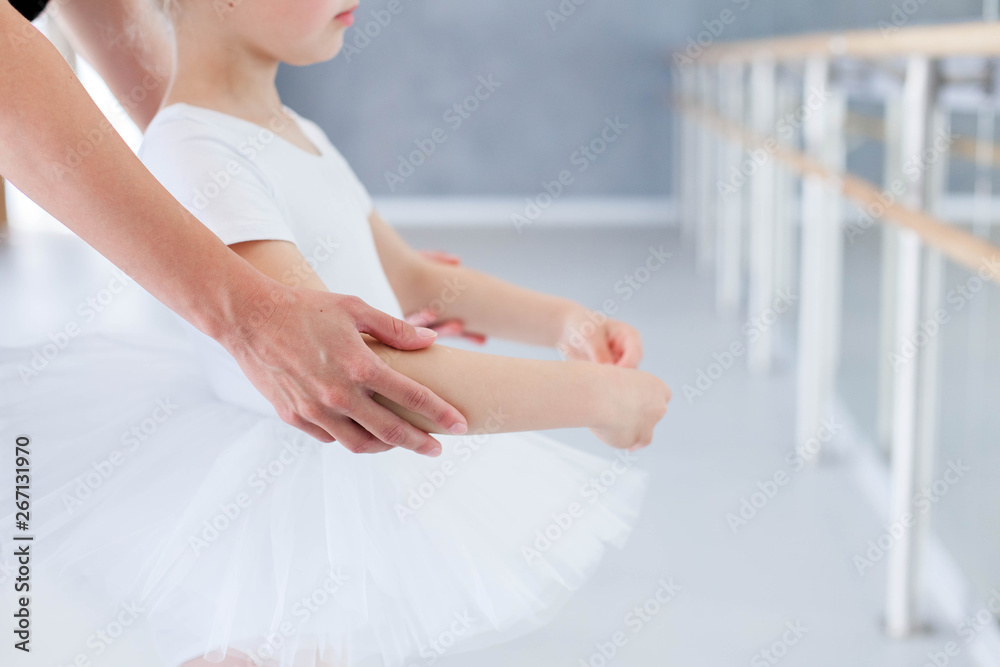 Little ballerina is studying with ballet teacher in classical dance school. Female dance trainer is teaching kid girl to do choreographic position with hands. Practicing for children. Close up. - obrazy, fototapety, plakaty 