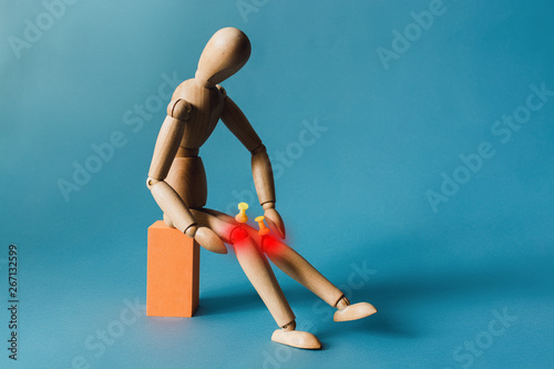 Joint pain concept. The wooden man holds his hands on sore red knee. photo