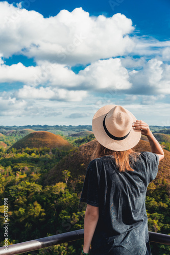Woman in straw hat standing in front of the Chocolate Hills in the Bohol island in the Philippines. Hills covered in brown grass. Famous touristic place © valeragf