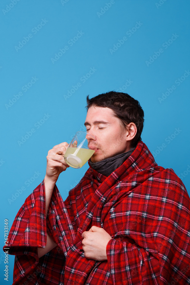 A wrapped in a blanket sick man is drinking from cup of medicine. A wrapped in a blanket sick man is drinking from cup of medicine.