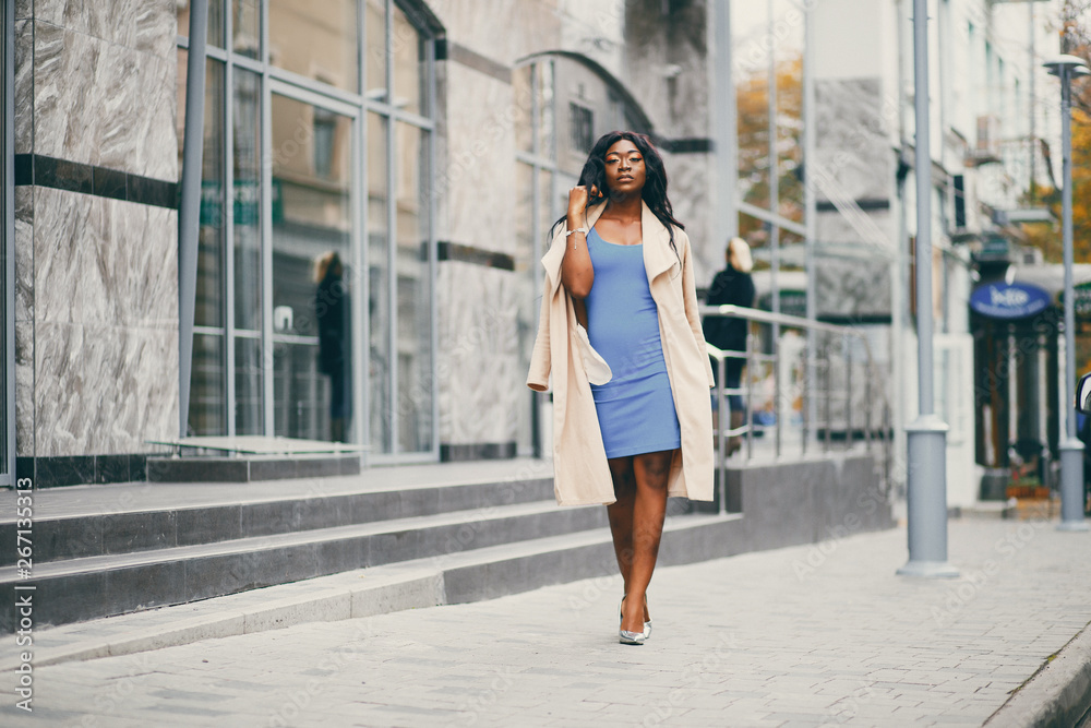 Elegant black woman standing in a autumn city. Businesswoman in a blue dress