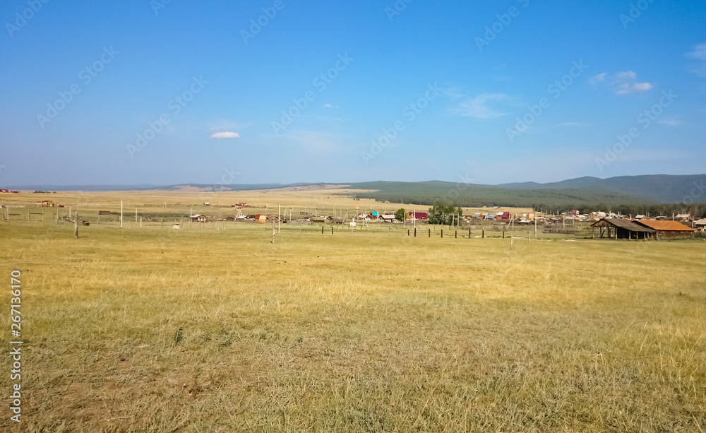  The shore of Lake Baikal. In the distance, wooden houses. Village. Summer landscape. Island Olkhon. Russia.