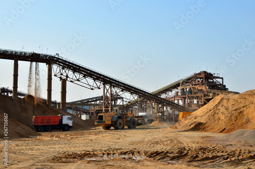 Wheel front-end loader unloading sand into heavy dump truck. Crushing factory, machines and equipment for crushing, grinding stone, sorting sand and bulk materials - Image