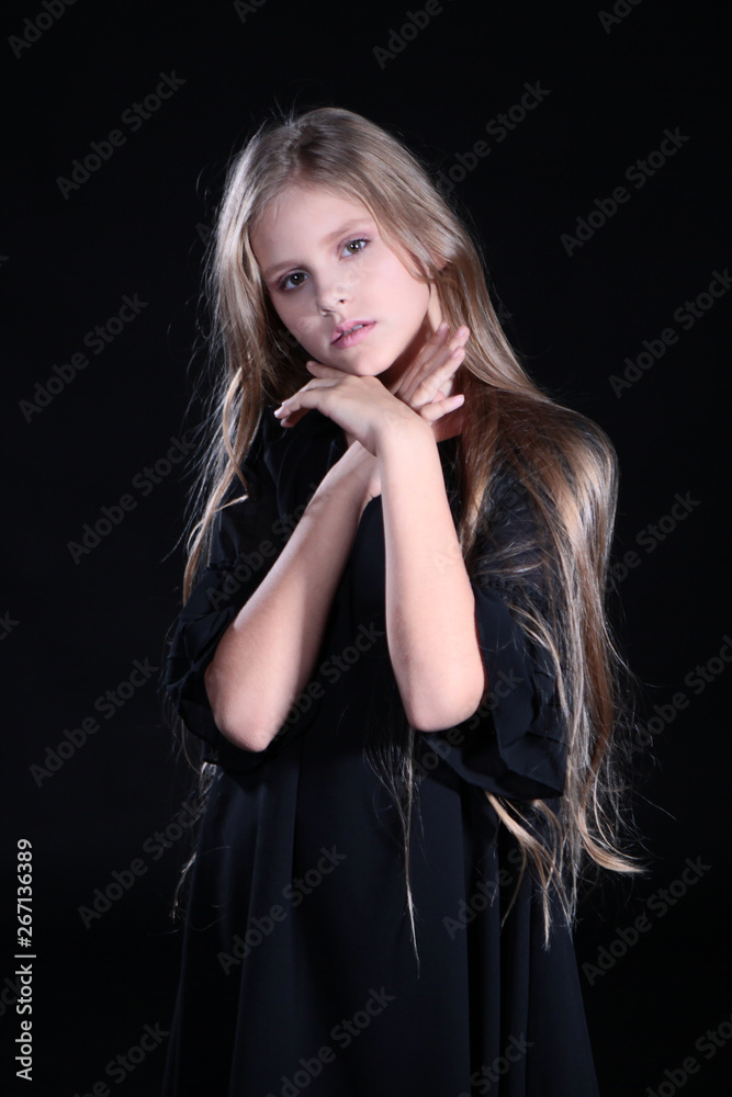 Portrait of a blonde girl with long hair on a black background. Emotional portrait.The girl shows different emotions on the face. Plays with long hair.