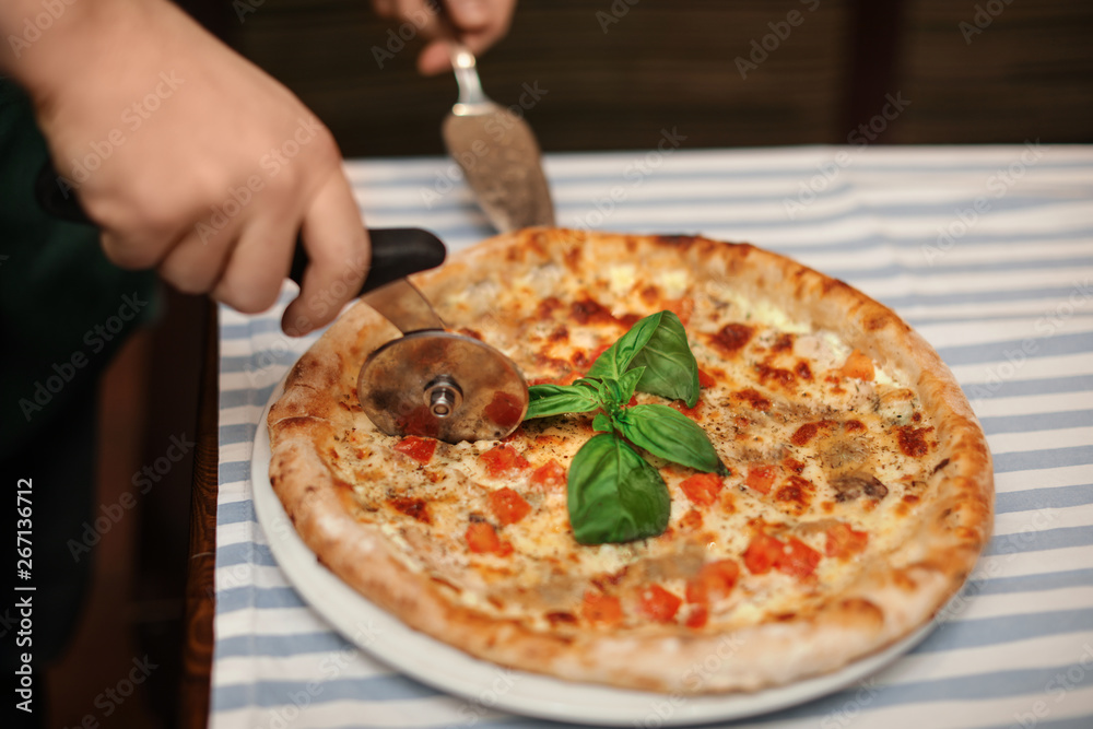 Man cutting tasty oven baked pizza on table, closeup Man cutting tasty oven baked pizza on table, closeup