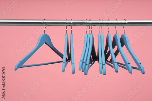 Empty clothes hangers on metal rail against color background