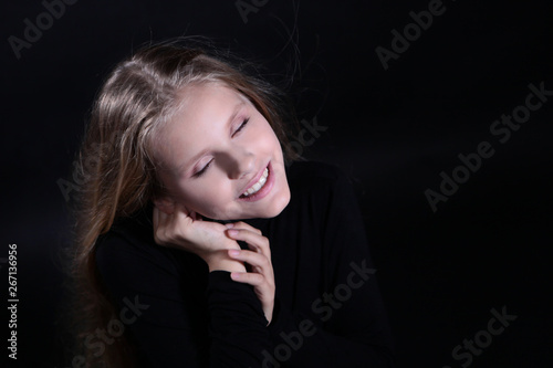 Portrait of a blonde girl with long hair on a black background. Emotional portrait.The girl shows different emotions on the face. Plays with long hair.