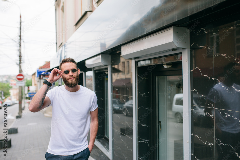 Handsome hipster man in sunglasses walking along the street. White t-shirt. Handsome hipster man in sunglasses walking along the street. White t-shirt.