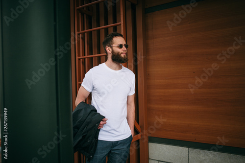 Handsome hipster man in sunglasses walking along the street. White t-shirt.