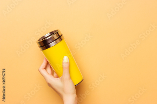 Female hand holding a yellow empty thermocup for drinks on a warm yellow background photo
