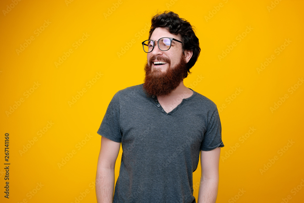 Portraito of cheerful smrat guy with beard smiling and looking away, over yellow background Portraito of cheerful smrat guy with beard smiling and looking away, over yellow background