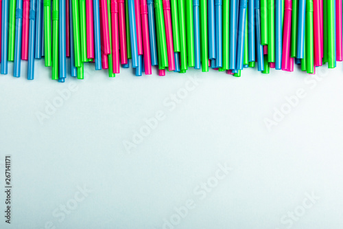 Plastic tubes. Multicolored cocktail straws lying on a green background with copy space for text. Top view.