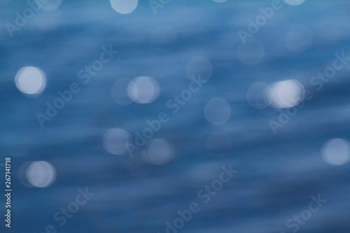 Bokeh lights on blue background. Bokeh bright, glowing, festive, waybill. Blurred river water with waves and bokeh light on a Sunny day. Blue blurred background.