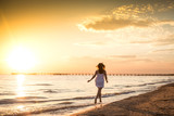 Slim young woman in white dress running on the beach at summer sunset