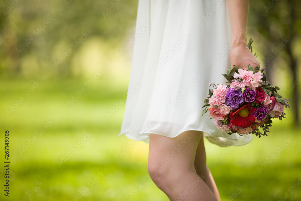 A woman in a cream-colored dress holding a beautiful wedding bouquet of flowers against a green park. Bride. A woman in a cream-colored dress holding a beautiful wedding bouquet of flowers against a green park. Bride.