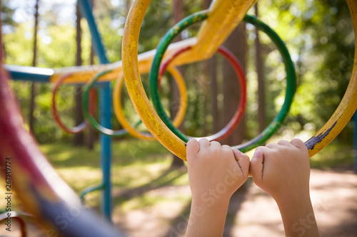 Young boy climbing on the playground during the summer. The child likes to climb the monkey bar on the playground in the fresh air. Little boy hands