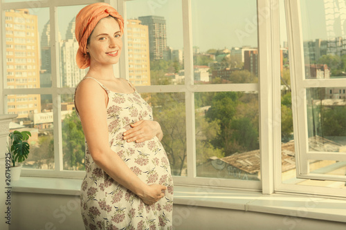 Beautiful pregnant woman standing near a large open window
