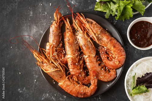 Fried grilled prawns with rice noodle, sauce and lettuce, dark background,copy space photo