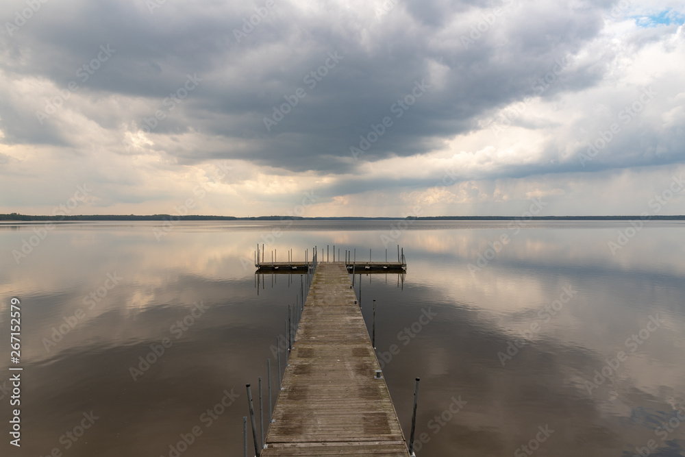A small bridge over the lake. Reflection of clouds on the lake's surface. - obrazy, fototapety, plakaty 