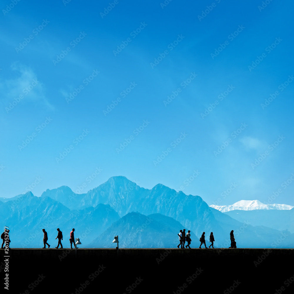 Fototapeta premium Silhouetted people walking on street over blue sky