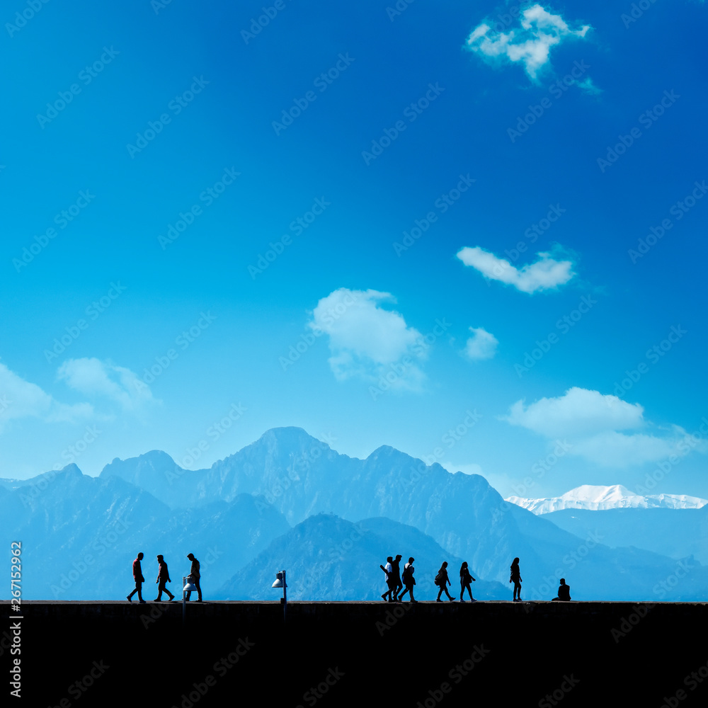 Silhouetted people walking on street over blue sky