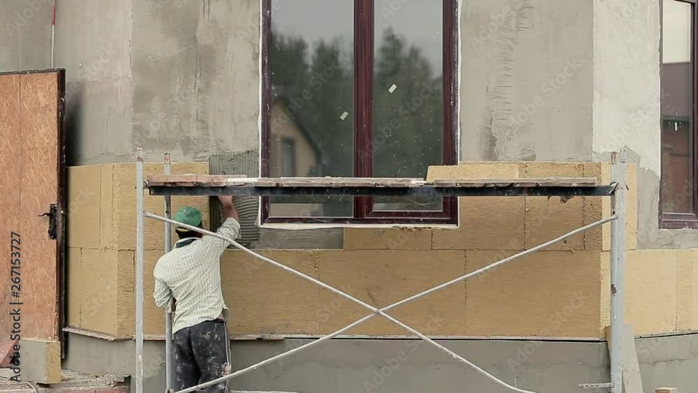 Worker man in white t-short and green baseboll insulates wall outdoor building