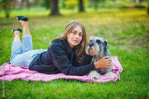 Pretty girl with his Schnauzer dog at nature park outdoor is standing and posing in front of camera. Portrait of owner and Rough collie dog enjoys, resting and petting together on city street.