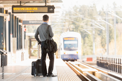 Businessman business traveler commuter with roller bag suitcase waiting on train station platform