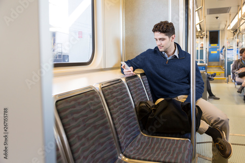 Young professional man commuter using cell phone riding on light rail subway train